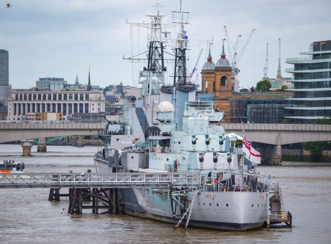 Historyczny okręt wojenny zacumowany na Tamizie z panoramą Londynu